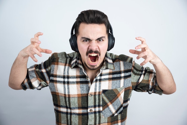 handsome man in headphones screaming on white wall.