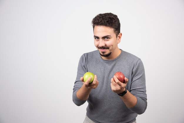 Handsome man holding apples on gray.