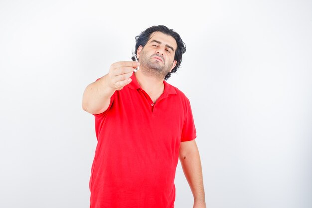 Handsome man holding cigarette in red t-shirt and looking serious. front view.