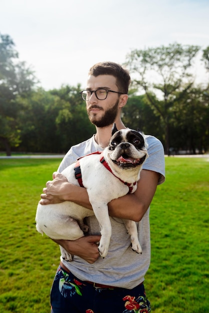 Foto gratuita uomo bello che tiene bulldog francese che cammina nel parco