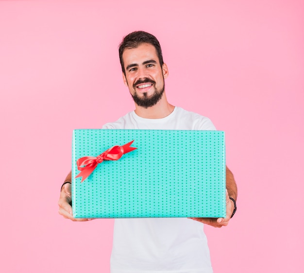 Handsome man holding gift box against pink background