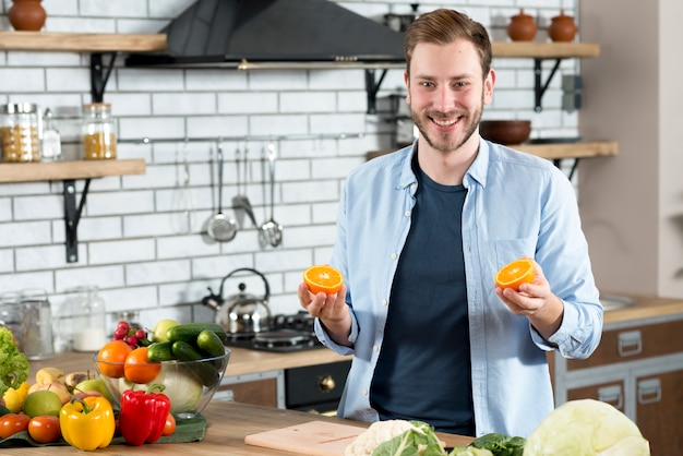 Uomo bello che tiene due fette di arance in cucina