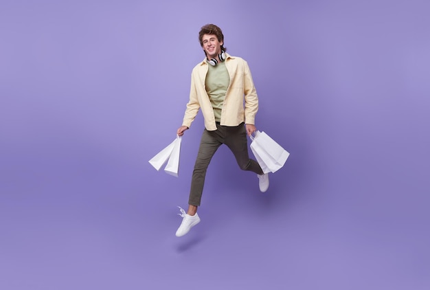 Handsome man jumping fast carry many bags rushing next shop store isolated over purple background