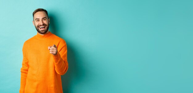 Handsome man laughing and pointing at camera nodding in approval agree with you standing over light