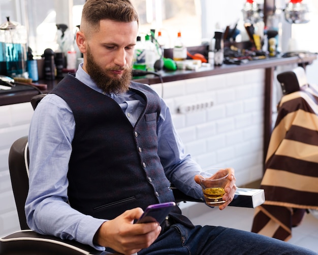 Handsome man looking on his phone at the barber shop