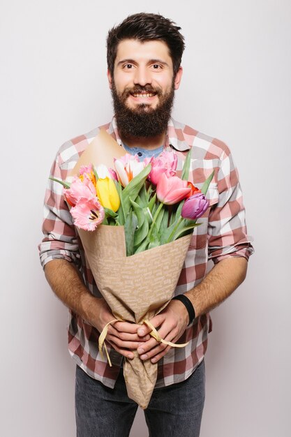 행복한 발렌타인 데이를 기원하는 사랑에 잘 생긴 남자, 낭만적 인 데이트에 꽃 꽃다발을주고, 웃고, 흰 벽 위에 양복을 입고