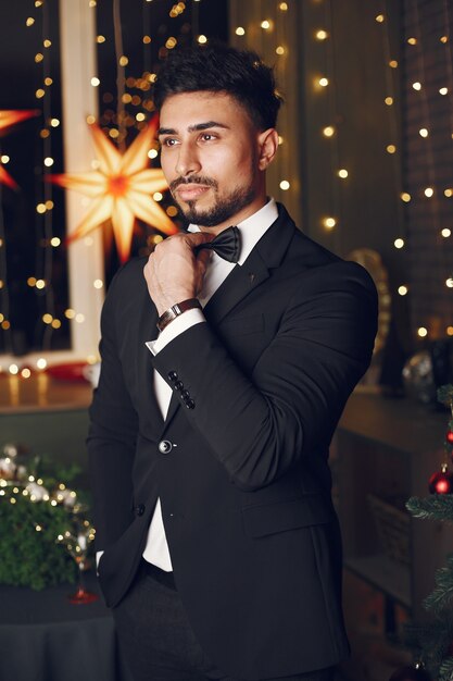 Handsome man near Christmas tree. Gentelman in a black suit.