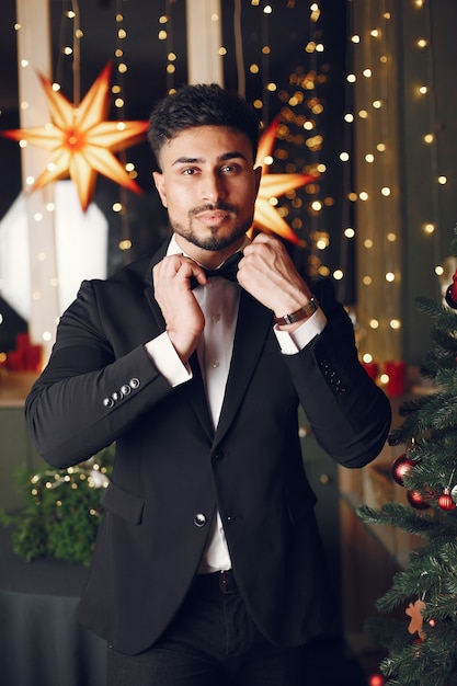 Handsome man near Christmass tree. Gentelman in a black suit.
