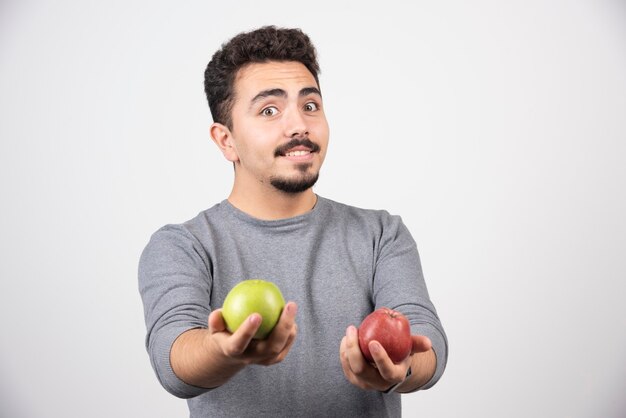 Handsome man offering apples on gray.