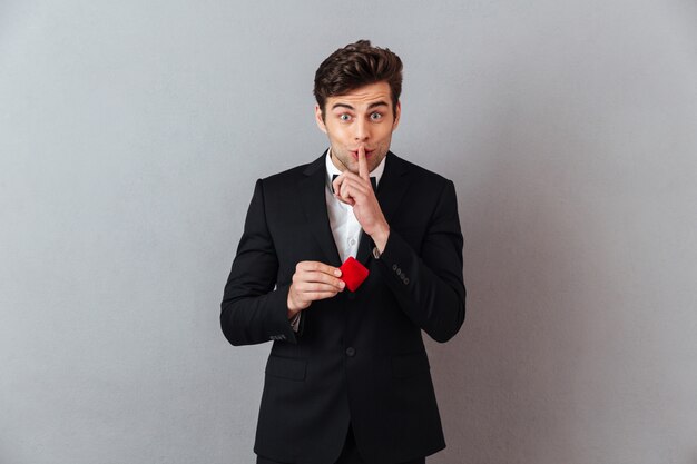 Handsome man in official suit holding box with proposal ring