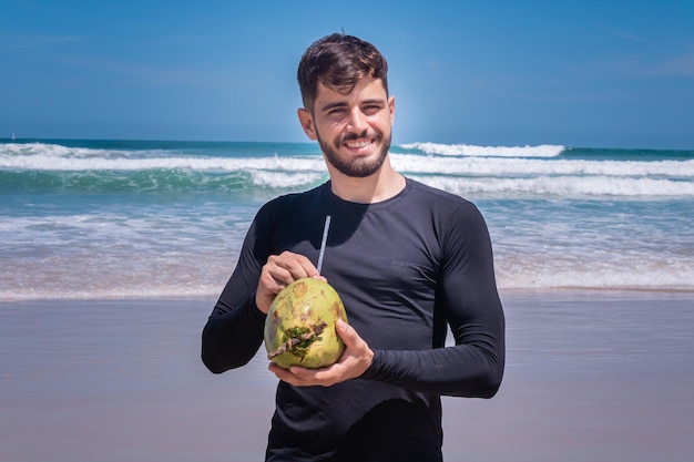 코코넛 물을 마시는 해변에서 휴가에 잘생긴 남자.