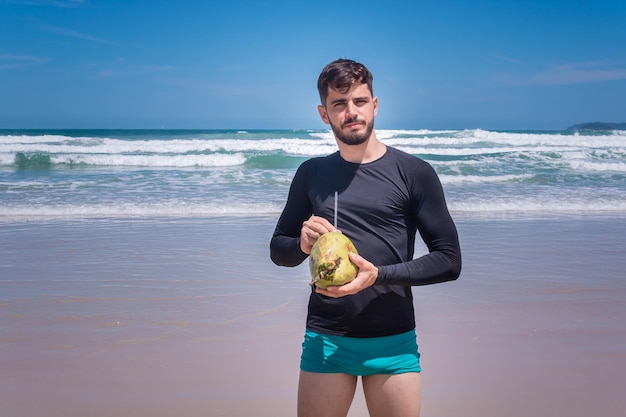 얼음 코코넛 물을 마시는 해변에서 휴가에 잘생긴 남자.