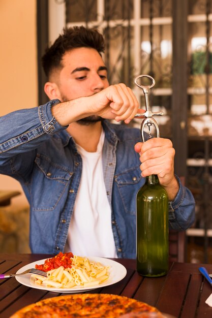 Handsome man opening alcohol bottle with opener