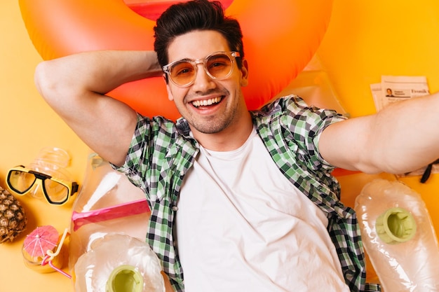 Handsome man in orange sunglasses is lying on inflatable mattress smiling and taking selfie