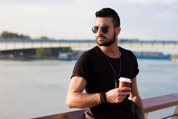 屋外でコーヒーを飲むハンサムな男。ひげそりを持つ男サングラス。 Instagramエフェクト。