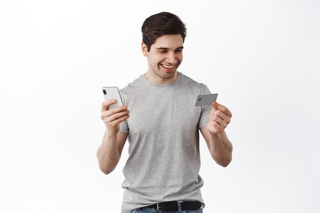 배경 위에 서 있는 인터넷 상점에서 앱 주문으로 신용 카드와 스마트폰 쇼핑으로 온라인으로 결제하는 잘생긴 남자