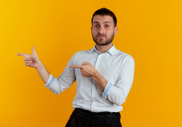 Handsome man points at side with two hands isolated on orange wall