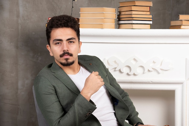 Handsome man posing serious over fireplace and books