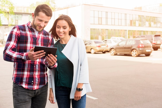 Free photo handsome man and pretty woman looking at digital tablet standing on street