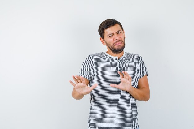 Handsome man raising hands to defend himself in t-shirt and looking scared. front view.