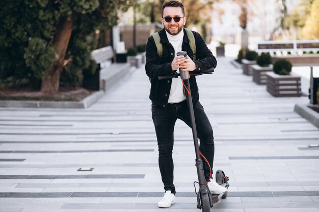 Handsome man riding on scooter and drinking coffee from thermos