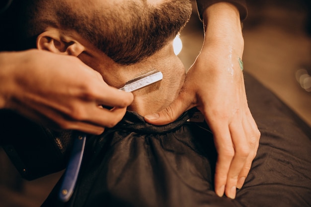 Красивый мужчина бреет бороду в парикмахерской