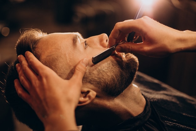 Красивый мужчина бреет бороду в парикмахерской