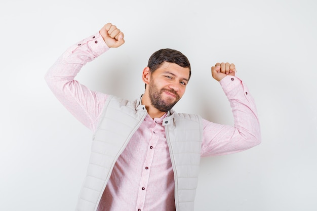 Handsome man showing winner gesture in vest, shirt and looking victorious.