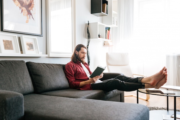 ハンサムな男が座って、自宅のソファーで本を読んで
