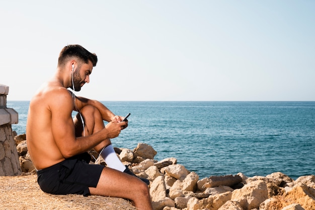 Foto gratuita uomo bello che si siede sulla spiaggia