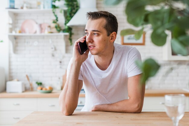 Uomo bello che parla dal telefono in cucina