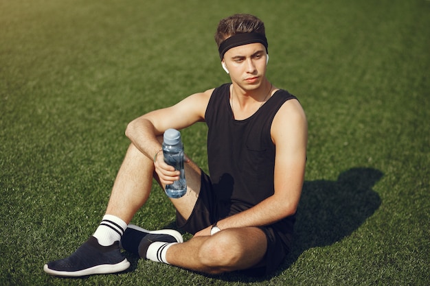 Красивый мужчина в спортивной одежде питьевой воды в парке