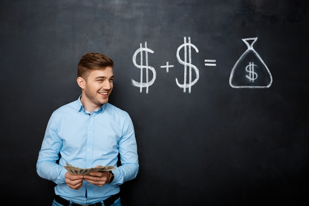 Handsome man standing over blackboard  with drawn dollar concept