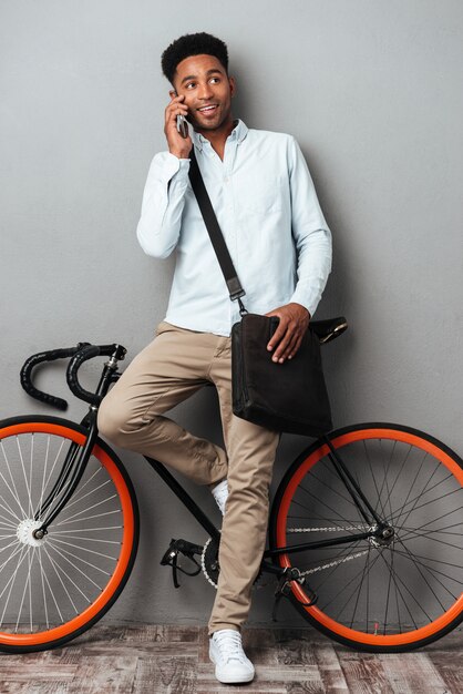 Handsome man standing near bicycle talking by phone.