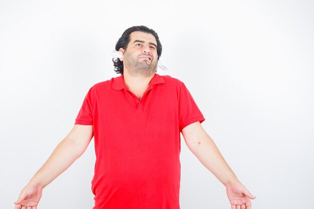 Handsome man standing with napkins in ears in red t-shirt and looking puzzled , front view.