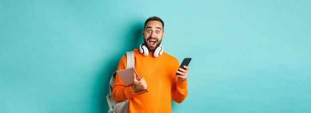 Foto gratuita bell'uomo studente con cuffie e zaino in possesso di tablet digitale e smartphone dall'aspetto fantastico