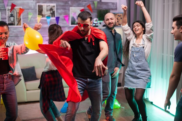 Handsome man in superhero costume dancing on disco music at friends party.