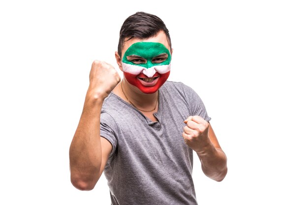 Handsome man supporter fan of Iran national team painted flag face get happy victory screaming into a camera. Fans emotions.