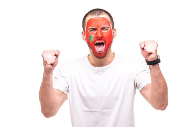 Handsome man supporter fan of Morocco national team painted flag face get happy victory screaming into a camera. Fans emotions.