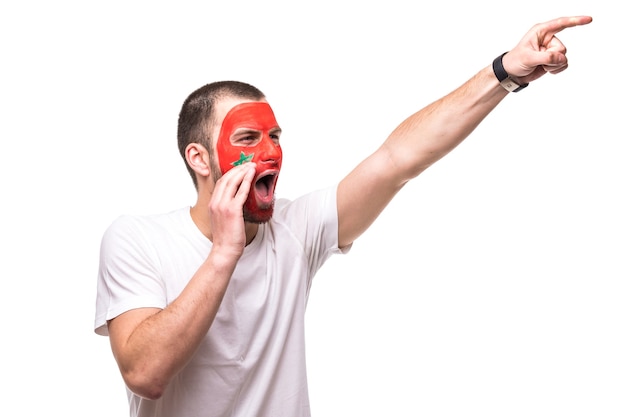 Free photo handsome man supporter fan of morocco national team painted flag face get happy victory screaming pointed with hand. fans emotions.