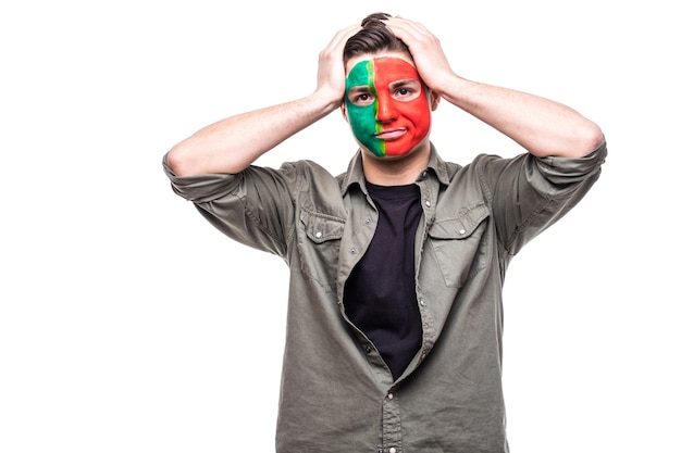 Free photo handsome man supporter fan of portugal national team painted flag face get unhappy sad frustrated emoitions into a camera. fans emotions.