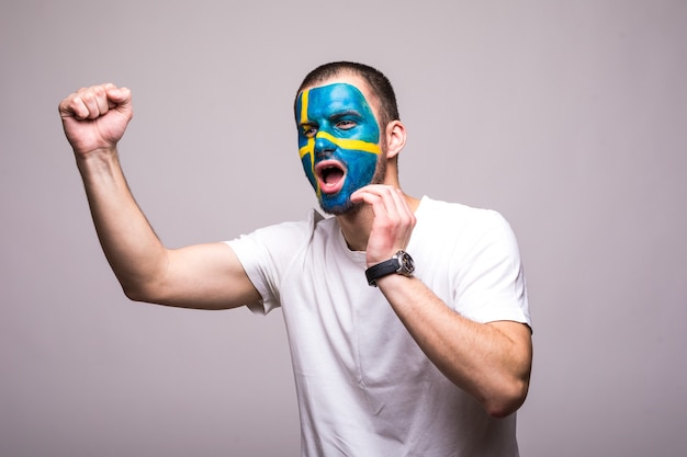 Handsome man supporter fan of Sweden national team painted flag face get happy victory screaming pointed hand. Fans emotions.