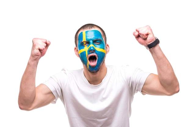 Foto gratuita il fan del sostenitore dell'uomo bello della squadra nazionale della svezia con la faccia dipinta della bandiera ottiene la vittoria felice che grida in una macchina fotografica. fans le emozioni.