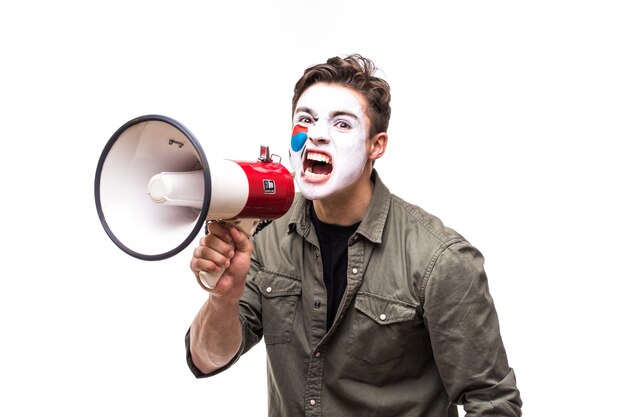 Handsome man supporter loyal fan of Korea Republic national team with painted flag face screaming into megaphone with pointed hand. Fans emotions.