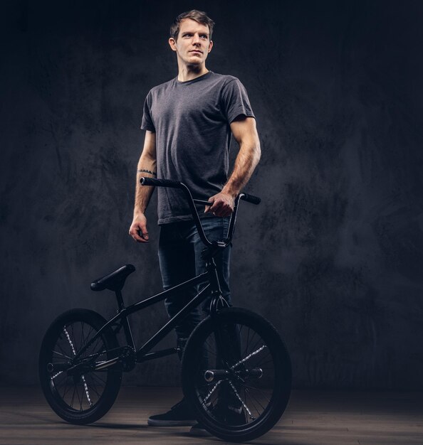 Handsome man in t-shirt and jeans standing with BMX. Isolated on a dark background.