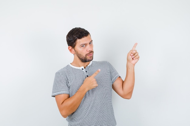 Free photo handsome man in t-shirt pointing at upper right corner and looking confident , front view.