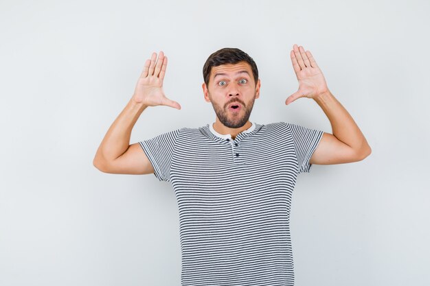 Handsome man in t-shirt showing palms in surrender gesture and looking astonished , front view.