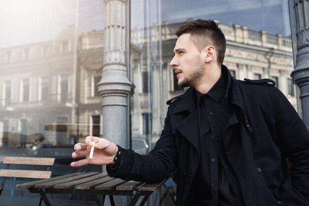 Handsome man in total black having cigarette, looking away.