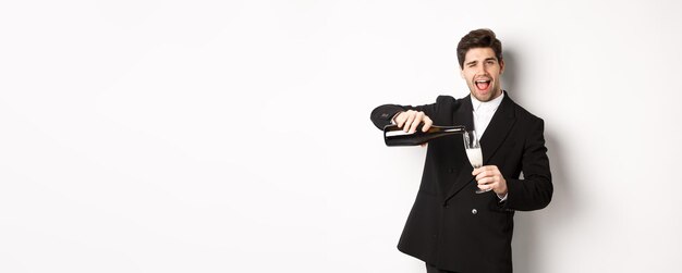 Handsome man in trendy suit pouring glass of champagne celebrating christmas smiling amazed and havi