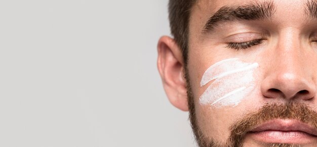 Handsome man using face cream while having his eyes closed